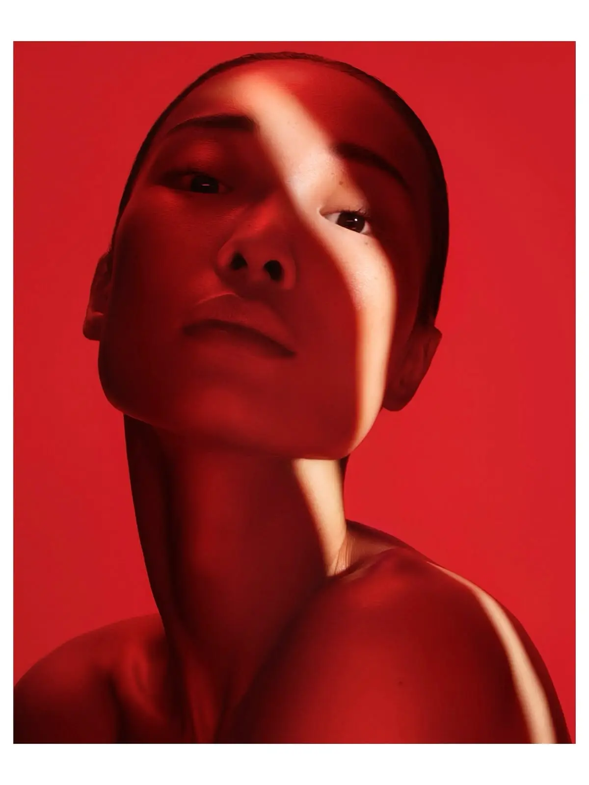 Editorial portrait of a woman lit entirely in deep red light against a red background, a single pale beam crossing her face