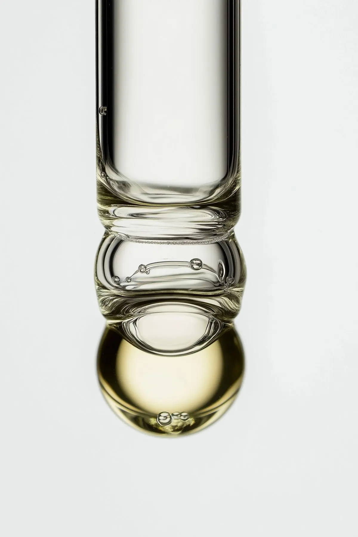 Macro photograph of a glass vial holding a pale yellow serum, lit against a plain background